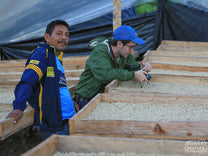 Raul Hector Trujillo (left) stands next to his drying coffee while Pedro (right) snaps photos.