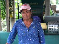 Farmer Maria Ilma poses for a photo in front of her green pulper and blue tiled fermentation tanks at her farm.