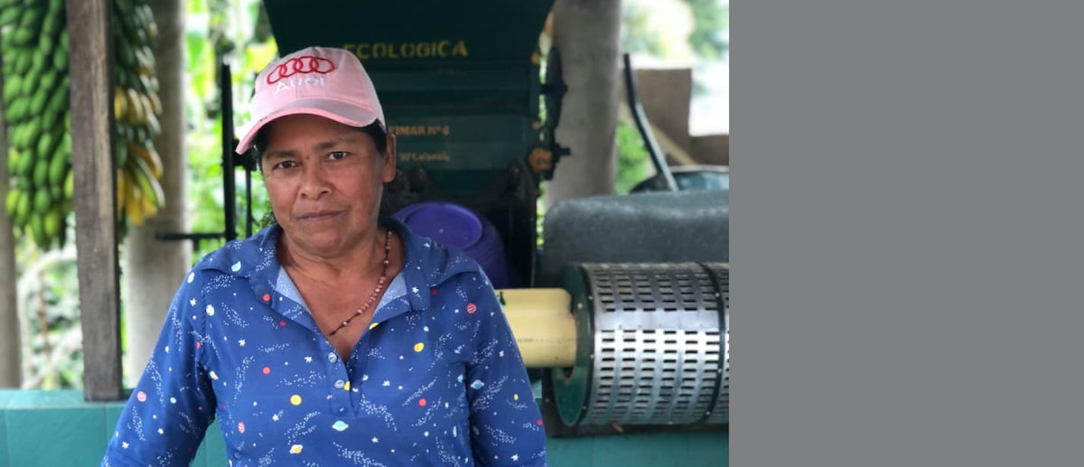 Farmer Maria Ilma poses for a photo in front of her green pulper and blue tiled fermentation tanks at her farm.