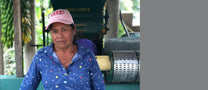 Farmer Maria Ilma poses for a photo in front of her green pulper and blue tiled fermentation tanks at her farm.