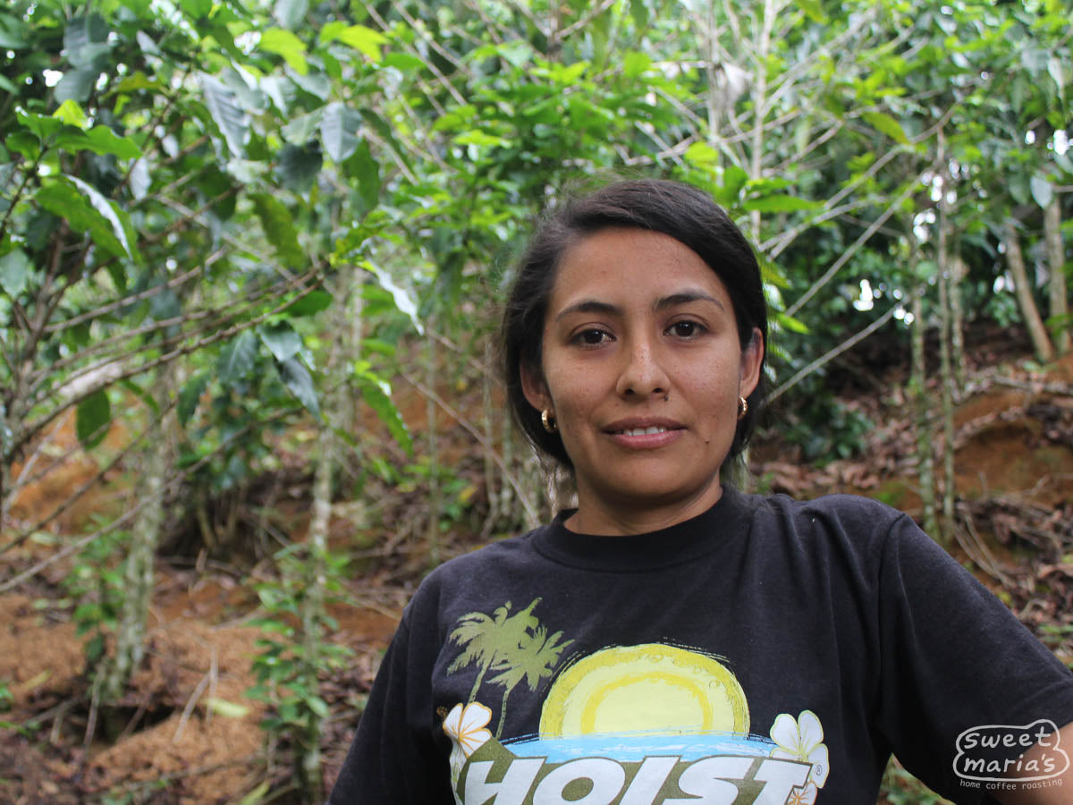Sara Chinchilla poses for a photo in front of her green coffee shrubs in Las Flores, Honduras.