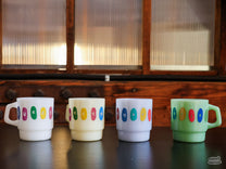 The Sweet Maria's Milk Glass Mug is adorned with our pebble logo design in jewel tones.