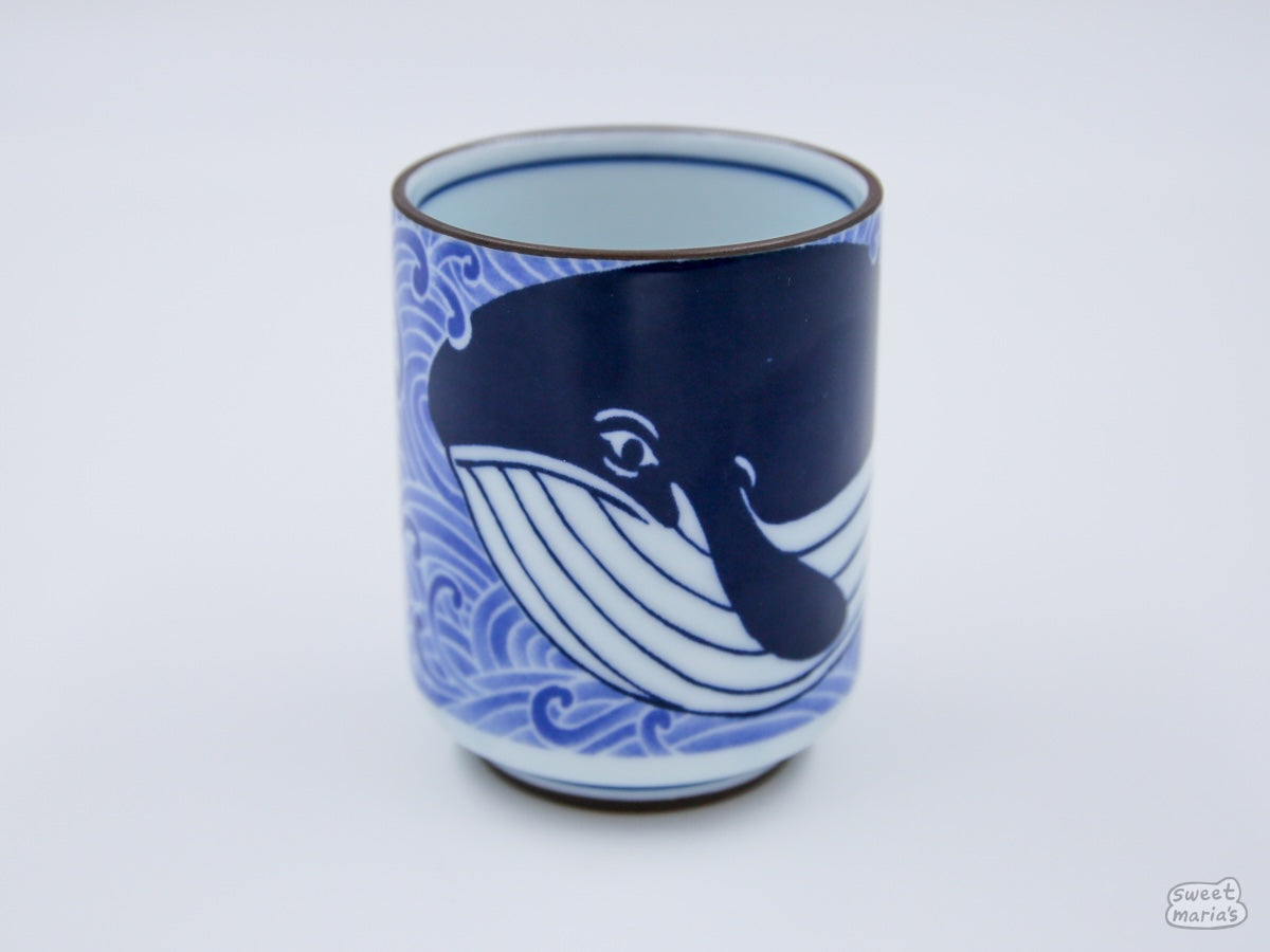 The Sad Whale Ceramic Cup is adorned with indigo blue whales swimming through water.