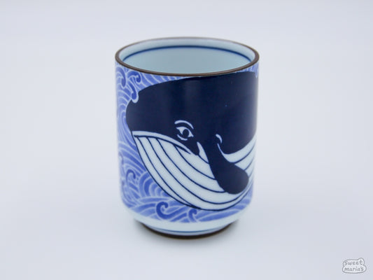 The Sad Whale Ceramic Cup is adorned with indigo blue whales swimming through water.