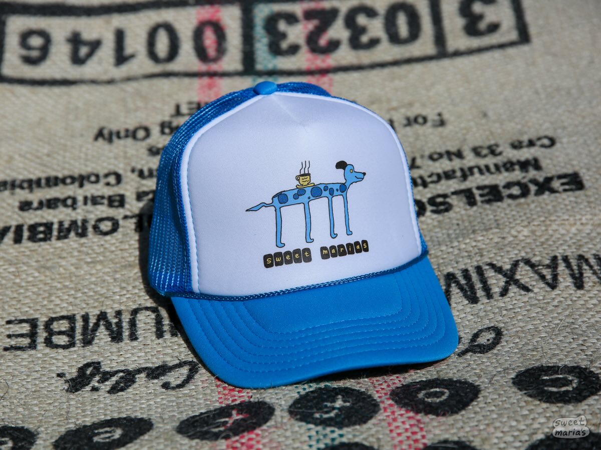 The Blue Chucho Summer Camp Hat features a spotted blue chucho serving up a hot cup of coffee.