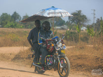 Boda Boda motorcycle taxi with an umbrella for shade on a dirt road in Tanzania.