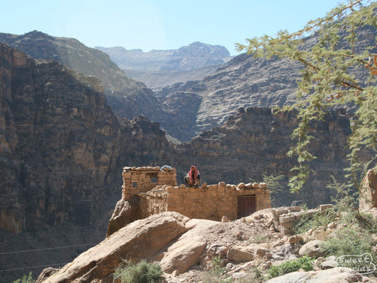 A man sits atop a stone wall on a rocky outcropping in Saih valley region of Sana's, Yemen.